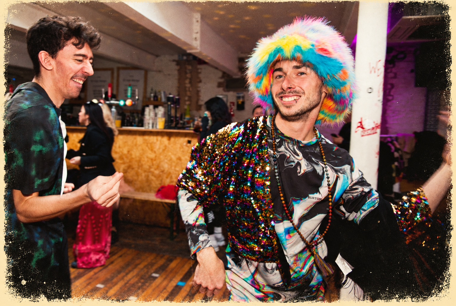 Two smiling dancers in colourful party clothes, with a softly distressed vintage print finish